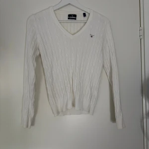 Vit kabelstickad tröja från Gant - Vit kabelstickad tröja från Gant i stretchig bomull. Klassisk v-ringning och diskret Gant-logga på bröstet. Långärmad modell med ribbade muddar och en clean, tidlös look som passar perfekt till jeans eller kjol. Pris kan diskuteras💗