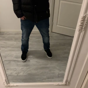 Svart pufferjacka från Burberry XL - Säljer en svart pufferjacka från Burberry i storlek XL. Jackan har klassiskt rutigt foder, huva och dragkedja framtill. På bröstet finns Burberrys logga i guld och på ärmen en patch med texten 'Burberry London England'. Perfekt för kalla dagar.