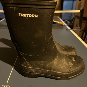 Svarta barn-gummistövlar från Tretorn - Svarta klassiska gummistövlar från Tretorn med robust sula och diskret logga på sidan. Storlek 33. Gott brukaskick.