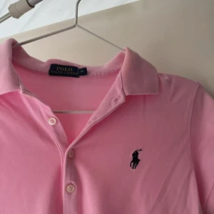 Ralph Lauren Rosa pikétröja  - Polo Ralph Lauren Storlek M  Använd ett par gånger  Köpt på en outlet i USA. Snygg rosa pikétröja från Ralph Lauren med klassisk krage och knäppning framtill. Tillverkad i mjuk bomull som är skön mot huden.