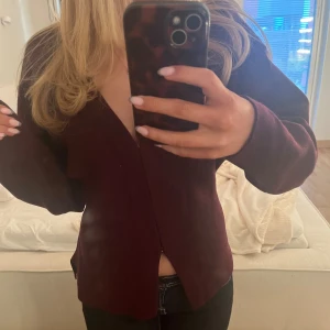 Vinröd kofta med v-ringning - Vinröd kofta med djup v-ringning och lång ärm. Modellen är rak och lite loose, perfekt att slänga på sig över ett linne eller t-shirt. Materialet känns mjukt och koftan är enkel utan synliga knappar eller dragkedja.