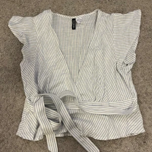 Randig omlottopp från H&M Divided - Säljer en ljusblå och vit randig omlottopp från H&M Divided. Aldrig använt ❤️