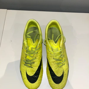 Nike Hypervenom gula fotbollsskor - Säljer ett par Nike Hypervenom fotbollsskor i en riktigt skarp gul färg med svarta och turkosa detaljer. Skorna har snörning, mönstrad ovandel och dobbar för gräsplan. Perfekta för dig som vill sticka ut på planen och ha bra grepp.