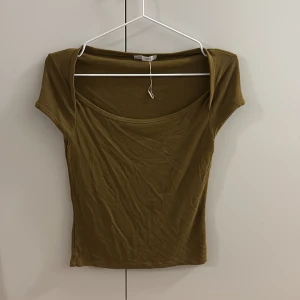 Olivgrön kortärmad topp - Snygg olivgrön topp med korta ärmar och rundad halsringning. Modellen är figurnära och passar perfekt till jeans eller kjol. Materialet känns mjukt och stretchigt, vilket gör den skön att bära. Enkel och stilren design som funkar till många olika looks.