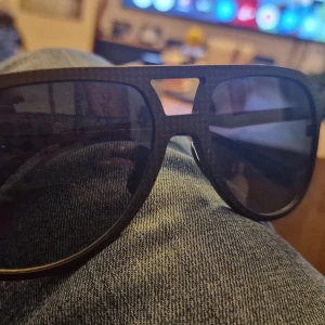 Svarta pilotbågar solglasögon - Snygga svarta solglasögon Oscar Eide Carbon pilotbågar och mörka glas. Ramen har en cool detalj med en metallfärgad brygga upptill. Perfekta för att ge en edgy vibe till din stil.