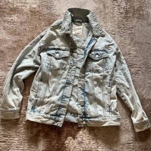 Ljusblå oversized jeansjacka Pull&Bear - Säljer en ljusblå jeansjacka från Pull&Bear med knappar framtill och bröstfickor. Jackan har en oversized form och slitna detaljer för en cool look. Perfekt att slänga över en t-shirt eller hoodie. Jättegullig ! Köpte för 600 kr. 