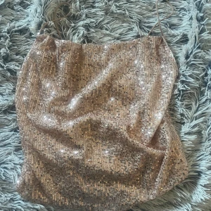 Champagnefärgad paljettlinne - Glittrig linne i champagnefärg med tunna axelband och täckt av paljetter. Perfekt för dig som vill sticka ut och glänsa på nästa fest. Snygg, figurnära passform och riktigt trendig look.