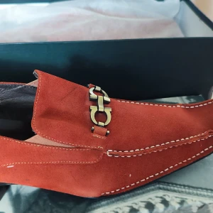 Bruna FIESSO mockaskor med låda av Aurelio Garcia storlek 10 - Perfekta för dig som vill sticka ut med stilrena detaljer och lyxig känsla.Nya FIESSO Skor med spänne från Aurelio Garcia, storlek 10. FIESSO by Aurelio Garcia, moderiktiga klänningsskor.  Nya oanvända. Slip-on-ovandel i mocka och mjuk, vadderad innersula i läder, vilket skapar en perfekt balans mellan mode och komfort. Ovandelmaterial: mocka, hälspänne. Foder: läder. Färg: Brun, Guld. Egenskaper: Strass. Bilderna visar den faktiska vara du får. 