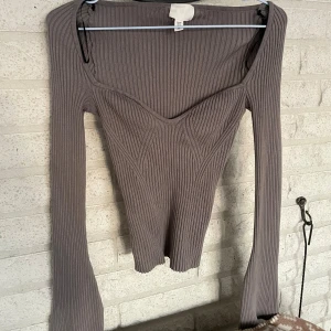  offshoulder topp - Säljer en grå ribbad offshoulder topp från H&M i storlek XS. Toppen har lång ärm, markerad byst och figurnära passform. Materialet är stretchigt och mjukt, perfekt för en trendig look. Snyggt v-ringad framtill och sitter tajt över kroppen. 