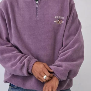 Urban Outfitters Lila fleece half zip  - Mysig lila fleece-tröja från Urban Outfitters med broderad logga på bröstet. Tröjan har half zip, hög krage och elastiska muddar vid ärmslut och nederkant. Perfekt för kyliga dagar och enkel att slänga på över en t-shirt. Storlek XS, lite oversieze så passar även dom som har M.