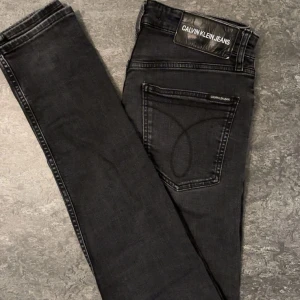 Svarta skinny jeans Calvin Klein - Svarta skinny jeans från Calvin Klein Jeans med klassisk femficksdesign, silverfärgade nitar och dragkedja. Snyggt broderad bakficka och tydlig logga på bakre läderpatch. Jeansen har smal passform och är tillverkade i stretchig denim.