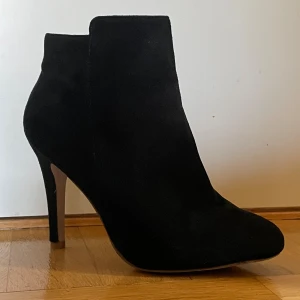 Svarta mocka stövletter med klack - Snygga svarta stövletter i mjuk mocka med smal hög klack och rund tå. Skorna har en stilren siluett och dragkedja i guld på sidan för enkel på- och avtagning. Perfekta för dig som gillar en elegant och modern look. Storlek 40 med 10 cm klack. Köpte dessa second hand för 450. Är villig att diskutera pris vid snabb affär 🥰🖤