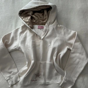 Krämvit hoodie från Freespirit med broderi - Snygg krämvit hoodie från Freespirit med blommigt broderi på fickan och insidan av huvan i glansigt material. Huvan har coola broderade detaljer och tröjan har en klassisk känguruficka. Perfekt för dig som gillar unika detaljer och mjuka material. Den är storlek 14 (ca 164 i barnstorlek), men passar storlek xs-s.