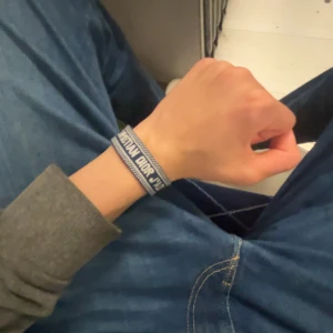 Blå Christian Dior J'Adior armband - Snyggt blått tygarmband från Christian Dior med texten 'J'Adior' broderad i vitt. Armbandet har ett justerbart knytband och detaljerade kanter i vitt. Perfekt accessoar för dig som gillar exklusiva märken och vill sticka ut med en trendig look.