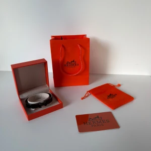 Svart armband från H Paris - Stilrent svart armband från H Paris med klassisk H-detalj. Kommer i original ask, påse och med äkthetskort. Armbandet har en elegant och minimalistisk design som lyfter vilken outfit som helst.