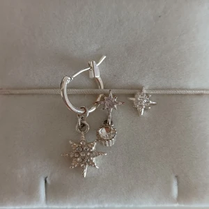 Silvriga örhängen med stjärnberlocker - Säljer ett set silvriga örhängen med flera stjärnformade berlocker och en glittrig sten. Örhängena har en cool och trendig vibe med små detaljer som gnistrar. Perfekt för dig som gillar att sticka ut med unika smycken och älskar stjärnmotiv. Kommer till båda öronen såklart!<3