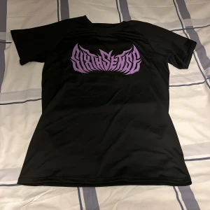 Svart t-shirt med lila tryck - Svart t-shirt från Sixth Sense med ett stort lila grafiskt tryck på bröstet. T-shirten har klassisk passform, rund hals och är tillverkad i ett mjukt, syntetiskt material som känns svalt mot huden. Perfekt för dig som gillar streetwear och vill sticka ut. Denna används i någon slags träning, varan är commpressed och är i storlek s/m