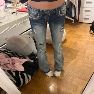 Blå bootcut jeans från Twentyone Black - Snygga blå jeans med bootcut från Twentyone Black. De har slitna detaljer, patchar och coola broderier på fickorna. Låg midja och kontrastsömmar ger en edgy vibe. Perfekt för dig som gillar statement-jeans med unik look.