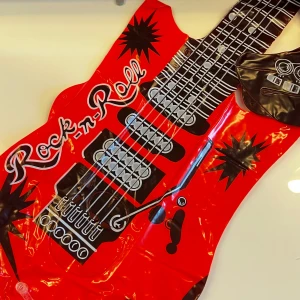 Uppblåsbar Rock-n-Roll Gitarr & Röda Nätvantar - Uppblåsbar gitarr med rock-n-roll design i rött och svart, perfekt för halloween eller liknande  temafest. Inkluderar ett par röda nätvantar i 80-talsstil. Båda i fint skick, inga synliga defekter. (Obs, gitarren har blivit uppblåst en gång så rekommenderar att man har ballongpump eller liknande hemma)