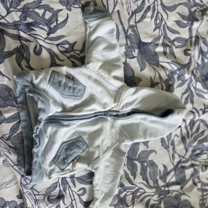 4-pack babytröjor i neutrala färger - Säljer fyra söta babytröjor: en ljusgrå hoodie med dragkedja och huva, en enkel ljusgrå sweatshirt, en vit långärmad tröja med små djurmotiv och en cremefärgad tröja med broderat kattansikte och öron. Perfekt för mysiga dagar och lek!