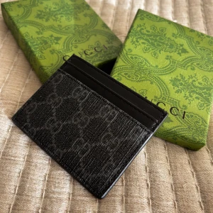 Svart Gucci korthållare  - Snyggt svart korthållare från Gucci, korthållare är tillverkat i en mix av skinn och textil. Perfekt för dig som vill ha en stilren och lyxig accessoar i fickan. OBS: Detta är inte en äkta Gucci korthållare men av top kvalitet. Det finns ingen skillnad på material, design eller box.