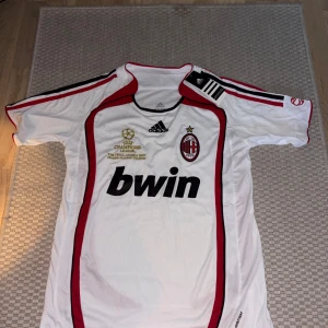 AC Milan Champions League 2007 tröja - Säljer en officiell AC Milan fotbollströja från Champions League-finalen 2007 i Aten. Tröjan är vit med röda och svarta detaljer, broderat klubbmärke och guldtext på bröstet. Adidas Performance, kortärmad och tillverkad i lätt polyester. Snyggt tryck med Bwin som sponsor.