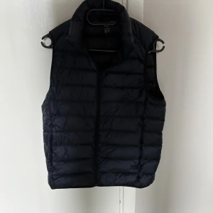 Mörkblå dunväst med dragkedja - Snygg mörkblå dunväst från Uniqlo. Lätt och smidig, perfekt för hösten över typ en hoodie. Nyskick, endast använd 1 gång. 