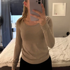 Tröja - En enkel och stilren beige långärmad tröja med rund halsringning. Tröjan har en slim passform och är tillverkad i ett mjukt och stretchigt material som sitter skönt på kroppen. Perfekt att matcha med jeans eller kjol för en clean look.