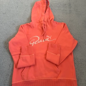 Korall hoodie från Puma med brodyr - Säljer en korallfärgad hoodie från Puma med broderad logga framtill. Tröjan har huva med snörning, magficka och ribbade muddar. Insidan är mjuk och fleecefodrad för extra komfort. Perfekt för kyliga dagar! Skriv om du vill veta något mer