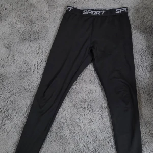 Svarta fleecefodrade leggings SPORT, S - Svarta leggings med fleecefoder och elastisk midja med SPORT-tryck. Tight passform och mjukt material som håller dig varm. Perfekta för träning eller chill dagar. Snygg och enkel design utan extra detaljer.