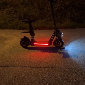 Elektrisk Scooter med Säte och LED-belysning - Kraftfull el-scooter med säte, LED-strålkastare och bakljus för säker körning i mörker. Digital display visar hastighet (upp till 49 km/h) och batterinivå. Snygg design, ser ut att vara i mycket gott skick utan synliga skador eller slitage.