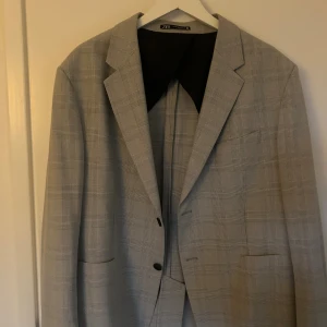 Grå rutig kostym från Zara - Snygg grå kostym från Zara med diskret rutigt mönster. Kavajen har klassisk krage, två knappar och fickor framtill. Byxorna matchar kavajen och har samma rutiga design. Perfekt för dig som gillar stilrena och moderna snitt.  Ordpris 2395kr 