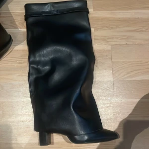 Svarta höga stövlar med klack - Give and shy likande Snygga svarta stövlar med hög klack och spetsig tå. Stövlarna har en slouchy passform och ett dekorativt band upptill. Perfekta för dig som vill ha en trendig och edgy look.