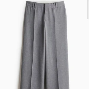 Grå wide kostymbyxor - Snygga grå kostymbyxor med breda ben och pressveck från H&M. Klassisk design med hällor för bälte och rak midja. Perfekta för en clean och stilren look, passar till skjorta eller t-shirt. Materialet känns mjukt och har en lätt struktur.
