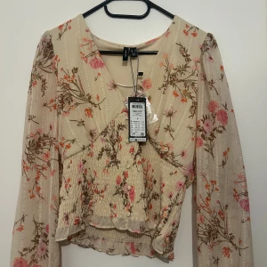 Blommig blus från Vero Moda - Supersöt blommig blus från Vero Moda i cremefärgad ton med rosa och orange blommor. Storlek M 