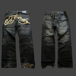 Ed Hardy jeans med stor logga bak - Sällsynta snygga mörkblå jeans från Ed Hardy med stor beige logga tryckt över bakfickorna. Klassisk femficksmodell med raka ben och bred passform. Köpta 2021 och de är i perfekt skick bortsett från längst ner, de har fått heeldrag men de gör de bara snyggare. 