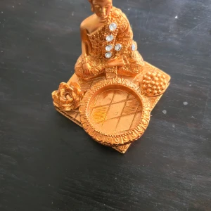 Buddha ljushållare - Ingen elektronikprodukt identifierad på bilderna. Objektet är en dekorativ staty i guldliknande färg med infällda stenar, inte en elektronisk enhet. Ingen synlig elektronik, märke eller modell. Inga defekter eller slitage synliga.