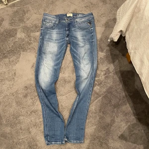 Replay Anbass jeans blå, storlek 31 - W31 L32.                                                     Snygga  Replay Anbass jeans i klassisk blå tvätt med slitningar och smal passform. Jeansen har fem fickor, dragkedja och knapp med Replay-logga. Bakfickorna har dekorativa sömmar och märkespatch. Perfekta för dig som gillar stilrena och moderna jeans.