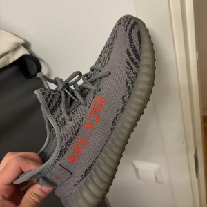 Adidas Yeezy Boost 350 V2 sneakers - Tre par Adidas Yeezy Boost 350 V2 sneakers säljes. En i grått med svarta detaljer och röd text, en svart med blå rand och text, samt en i beige och orange toner. Alla har stickad ovandel, snörning och den ikoniska ribbade sulan. Perfekta för dig som vill sticka ut med hypade sneakers.