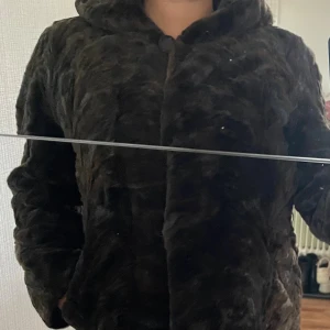 Brun pälsjacka - Brun faux fur jacka med knapp och små krokar för att stänga, luva och två sidofickor, passar Storlek S / 36