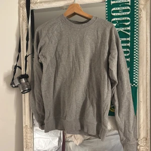 Grå sweatshirt från Neutral i bomull - En enkel och clean grå sweatshirt från Neutral i storlek S. Tröjan har rund hals, långa ärmar och är gjord i mjuk bomull. Perfekt för chill dagar eller när du vill ha en basic look. Passar dig som gillar minimalistisk stil.