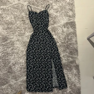 Blommig långklänning från Gina Tricot - Supersöt långklänning från Gina Tricot i marinblått med vita små blommor. Klänningen har smala axelband, figurnära passform och en snygg slits framtill. Perfekt för sommarens alla tillfällen! Storleken är xxs och den är true to size.