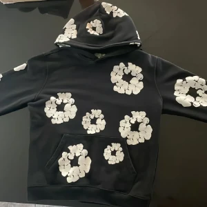 Svart hoodie och joggers med blommor - Säljer ett svart set med hoodie och joggers, dekorerade med stora vita blommiga tryck över hela plaggen. Hoodien har magficka och huva, byxorna har resår i midja och benslut. Perfekt för chill dagar och streetstyle.