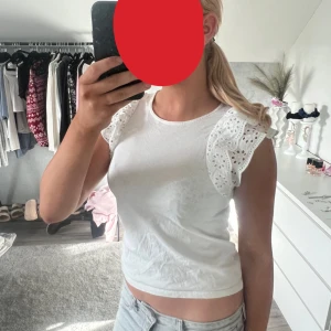Vit topp med broderade volangärmar - Säljer en söt vit topp med broderade volangärmar och rund halsringning. Toppen är croppad och har fina spetsdetaljer på ärmarna som ger en romantisk vibe. Perfekt för varma dagar och enkel att matcha med jeans eller kjol.