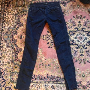 Replay Anbass mörkblå manchesterbyxor 31/36 - Snygga mörkblå manchesterbyxor från Replay, modell Anbass. Byxorna har klassisk femficksdesign, smal passform och midwaist. Materialet är mjuk manchester som ger en cool och lite retro känsla. Perfekt för dig som gillar stilrena och bekväma byxor. Midja 41cm längd 117cm (28)