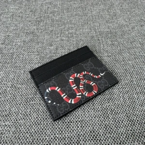 Korthållare - Svart plånbok  med ikoniskt GG-mönster och en cool röd, vit och svart ormprint på framsidan. Slimmad design med flera kortfack, perfekt för dig som vill ha stil och funktion i fickan. Materialet är slitstarkt skinn med tryckt mönster.