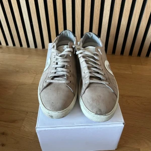 Beige sneakers från Oliver Cabell - Snygga beige sneakers från Oliver Cabell med vit sula och vit cirkeldetalj på sidan. Skorna har snörning, rund tå och svart hälparti med logga. Tillverkade i mocka och skinn för en clean och stilren look.