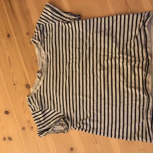 Randig t-shirt från H&M, vit/blå - Säljer en fräsch t-shirt från H&M i storlek S. Den är vit med smala mörkblå ränder och har klassisk rund hals. T-shirten är kortärmad och gjord i mjuk bomull, perfekt för en chill och stilren look.