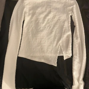 Vit och svart omlott topp med slits - Säljer två långärmade toppar i vit och svart med slits på sidan. Materialet är stretchigt och har en ribbad struktur