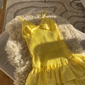 Gul kort sommarklänning med rosett - Superfin gul kort klänning med smala axelband, söt rosett på ryggen och volangig kjol. Storlek xs.